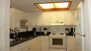 Una cocina compacta con alacenas blancas, una estufa y un refrigerador.