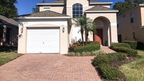 A two-story house with a garage, a large arched entrance, and a well-maintained front yard with hedges and a palm tree. - Mariner 1146 Apartment 4 Bedroom (Haines City)