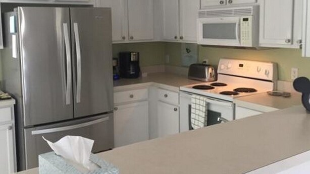 A kitchen with white cabinets, a stainless steel refrigerator, a microwave, and a stove. - Mariner 1146 Apartment 4 Bedroom (Haines City)