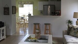 A living room with a white coffee table, a sofa, and a kitchen area in the background. - Mariner 1146 Apartment 4 Bedroom (Haines City)