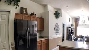 A kitchen with wooden cabinets, a black refrigerator, and a tiled floor. - St Kitts House Holiday home 4 Bedroom (Haines City)
