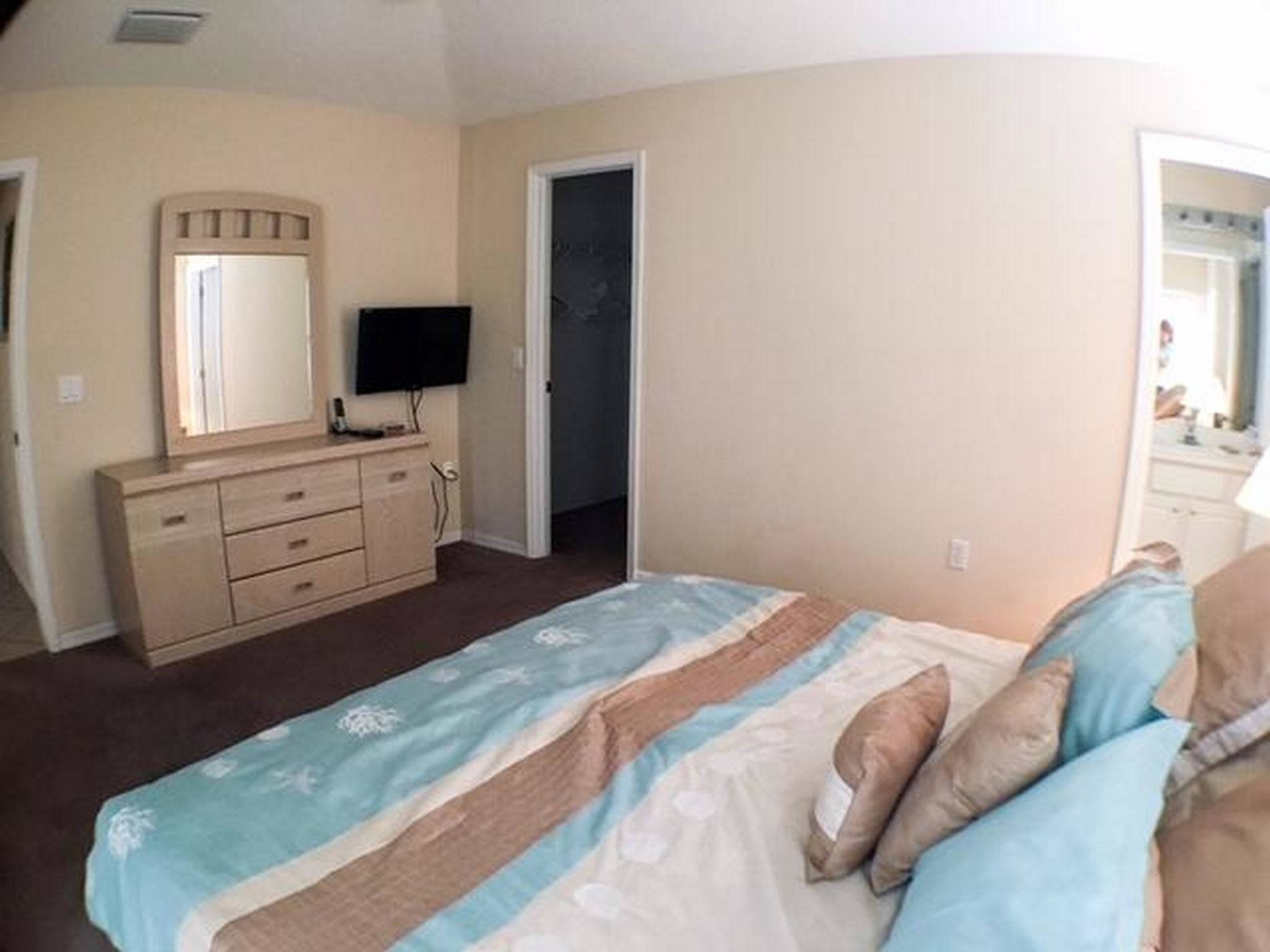Un dormitorio con cama, cómoda, televisor y puerta que da a otra habitación.
