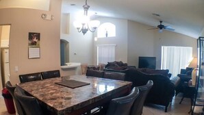 A dining area with a marble table and chairs, a sofa, and a TV in the background.