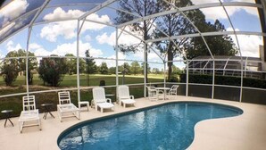 A covered outdoor swimming pool with white lounge chairs and a view of a golf course.