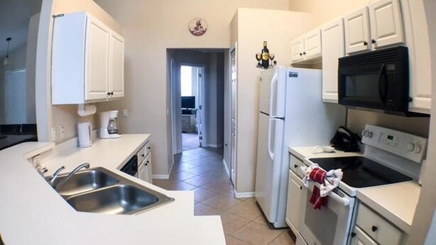 A modern kitchen with white cabinets, a stainless steel sink, a microwave, and an oven.