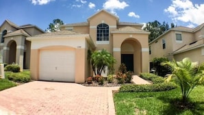 A two-story house with a garage, a central arched window, and a well-maintained lawn. - Mariner Pad Apartment 4 Bedroom (Haines City)