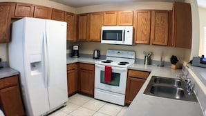 A kitchen with wooden cabinets, a white refrigerator, a microwave, a stove, and a sink. - Mariner Pad Apartment 4 Bedroom (Haines City)