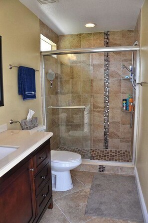 Un baño con ducha de vidrio, un inodoro blanco y tocador con espejo y perchero para toallas.