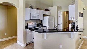 A compact kitchen with white cabinetry, a black countertop, and a built-in oven.