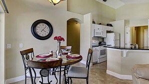 A dining area with a round table, chairs, a clock, and a vase with flowers.