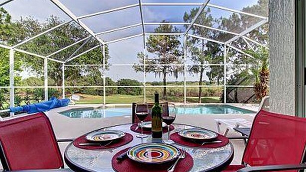 A covered outdoor area with a pool, red chairs, and a table set for dining.