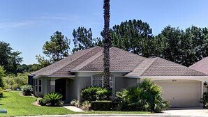A single-story house with a garage, surrounded by a well-maintained lawn and palm trees.