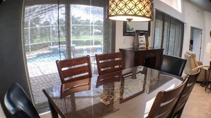 A dining area with a glass-top table, wooden chairs, and a pendant light. - Mallory Villa Villa 3 Bedroom (Haines City)