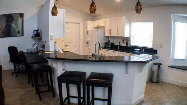 A modern kitchen with a central island, pendant lighting, and a dining area with bar stools. - Mallory Villa Villa 3 Bedroom (Haines City)