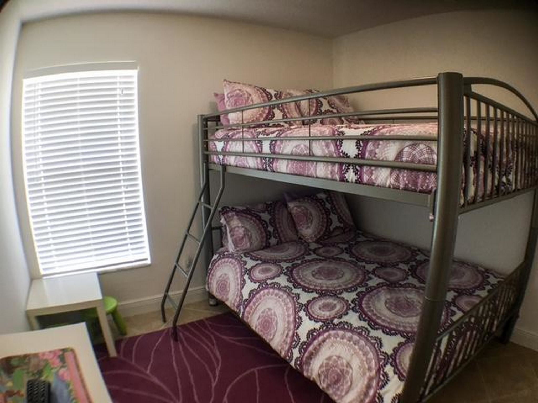 Een stapelbed met beddengoed met een patroon in een kamer met een raam en een klein tafeltje.