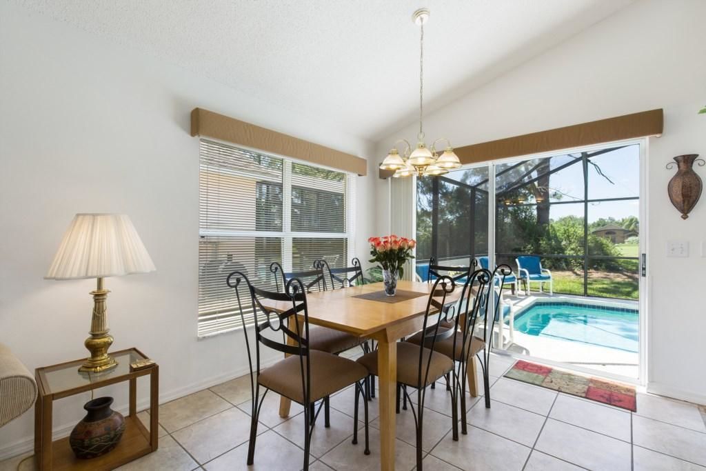 A dining area with a wooden table and chairs, a lamp, and a view of a swimming pool through large windows.