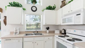Une cuisine moderne avec des meubles blancs, un four à micro-ondes encastré, une cuisinière et une fenêtre avec des stores.