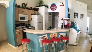 A kitchen with a bar area, a microwave, a refrigerator, and bar stools. - Park Place Retreat Apartment 4 Bedroom (Haines City)