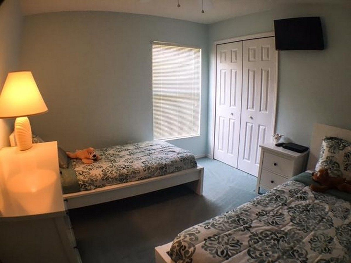 A bedroom with two beds, a nightstand, a lamp, a window with blinds, and a door.