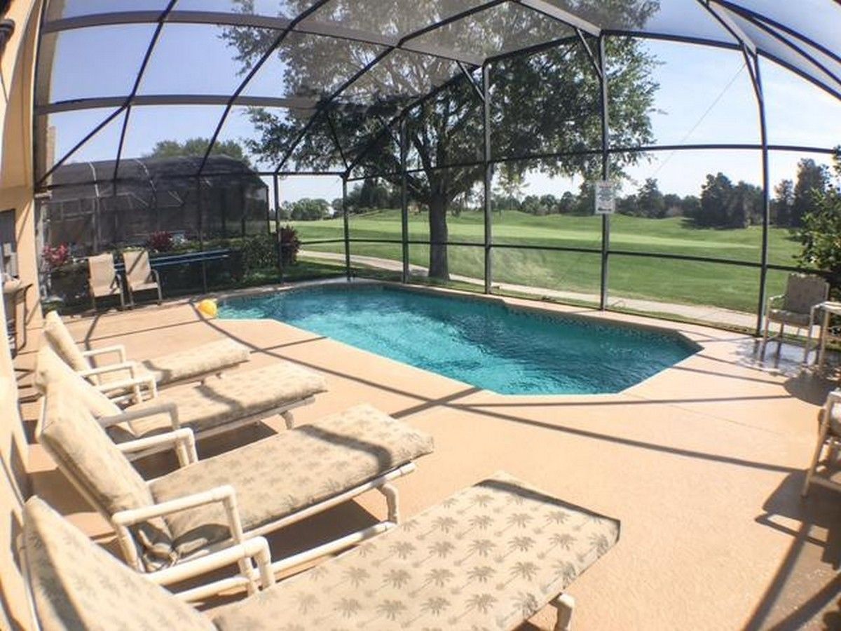 Un espace piscine avec des chaises longues et une vue sur un terrain de golf, le tout abrité par une structure couverte.