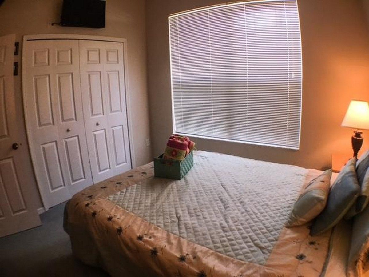 Een slaapkamer met een bed, een raam met zonwering, een deur en een bedlamp.