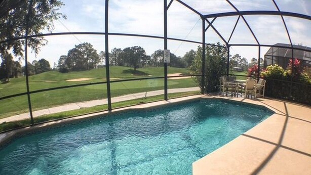 A clear swimming pool with a view of a golf course through a screened enclosure. - Park Place Retreat Apartment 4 Bedroom (Haines City)
