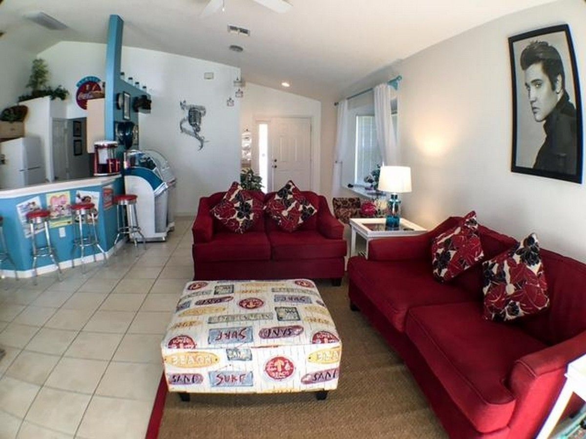 A living room with a red sofa, a patterned ottoman, and a bar area with stools.