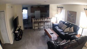 A living room with a black leather sofa, a coffee table, and a TV. There is a dining area with a table and chairs in the background. - Hemingway Golf View Apartment 4 Bedroom (Haines City)