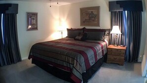 A bedroom with a bed, a nightstand, a ceiling fan, and a painting on the wall. - Hemingway Golf View Apartment 4 Bedroom (Haines City)