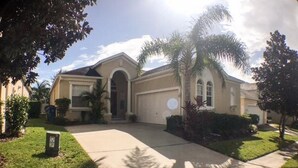 A two-story house with a garage, a front lawn, and a palm tree. - Calabay Dream Apartment 4 Bedroom (Haines City)