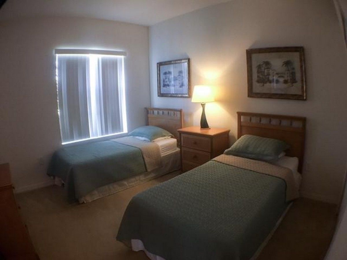 A room with two beds, a nightstand with a lamp, and two framed pictures on the wall.