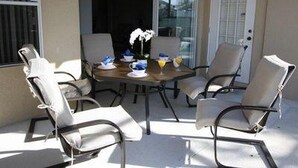 A patio with a round table and four chairs, a vase with flowers, and a door with a window. - Calabay Dream Apartment 4 Bedroom (Haines City)