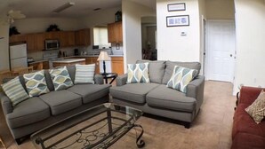 A living room with two grey sofas, a glass coffee table, and a red couch. - Kokomo 2749 Apartment 6 Bedroom (Haines City)