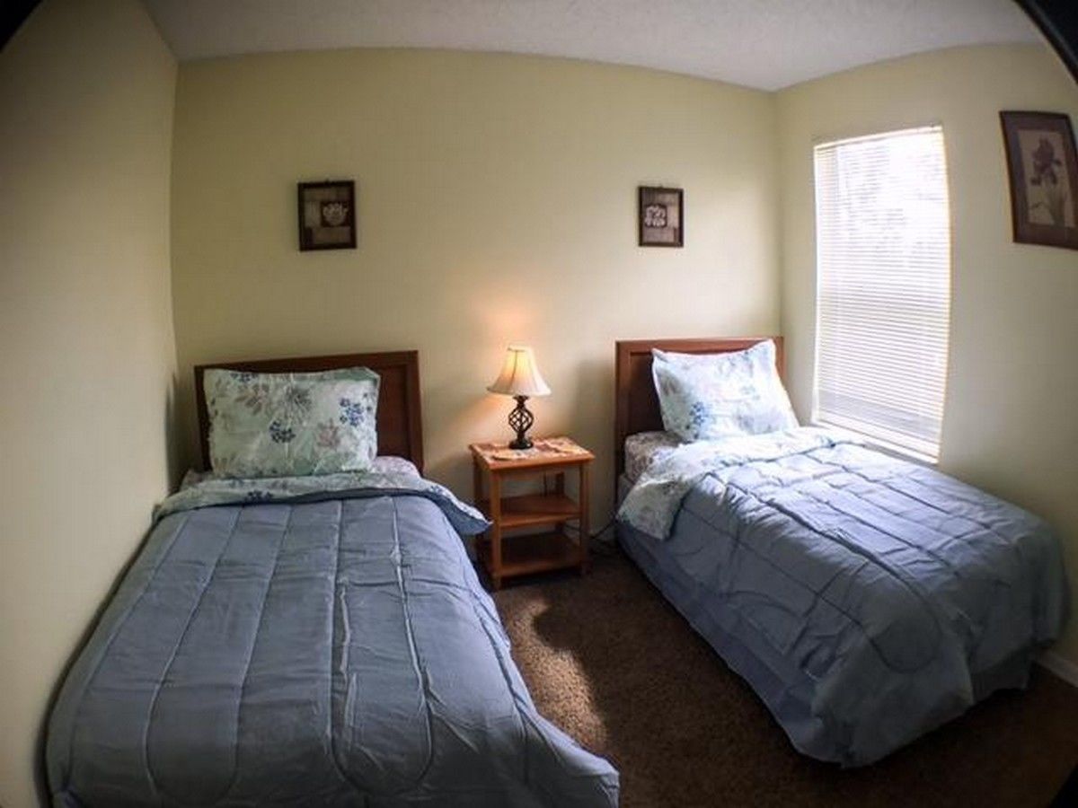 Un dormitorio con dos camas individuales, una mesita de noche con lámpara y una ventana con persianas.