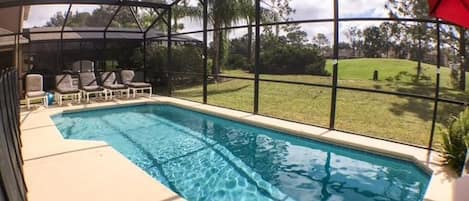 A swimming pool with a covered area, lounge chairs, and a view of a grassy landscape.