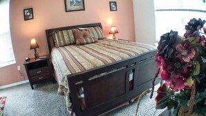 A bedroom with a bed, two bedside tables, a nightstand, and a large window. - Kokomo 2749 Apartment 6 Bedroom (Haines City)