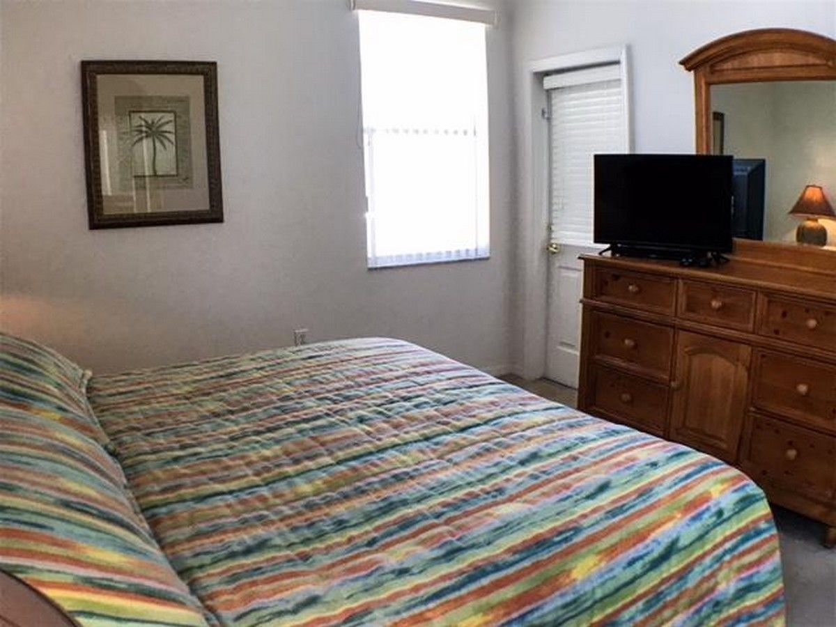 Une chambre à coucher avec un lit, une commode, un téléviseur et une fenêtre.