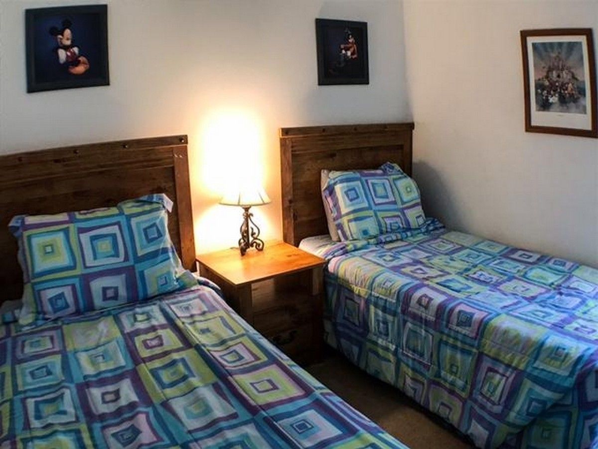 A room with two single beds, a nightstand with a lamp, and framed pictures on the walls.