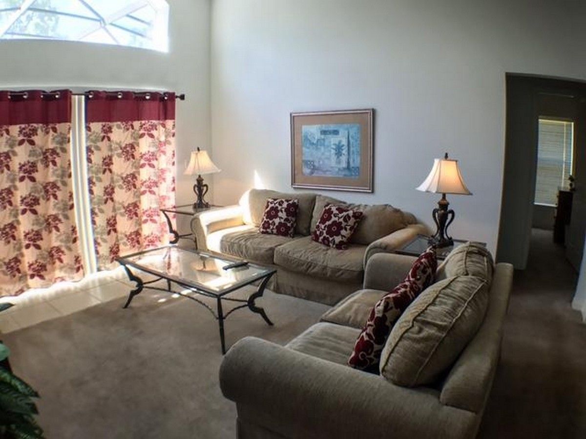 A living room with two sofas, a coffee table, and two lamps. There is a window with curtains and a framed picture on the wall.