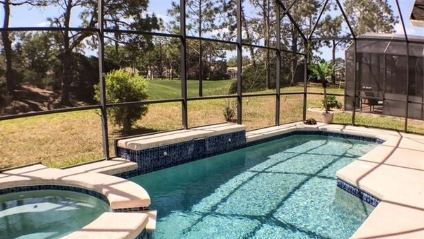 A swimming pool with a hot tub, surrounded by a covered patio area with a view of the backyard. - Kokomo Golf View Apartment 4 Bedroom (Haines City)