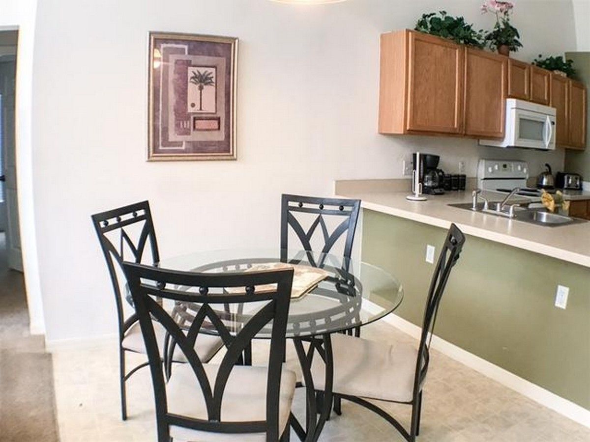 A compact kitchen with a round glass table and four chairs, a microwave, and wooden cabinets.