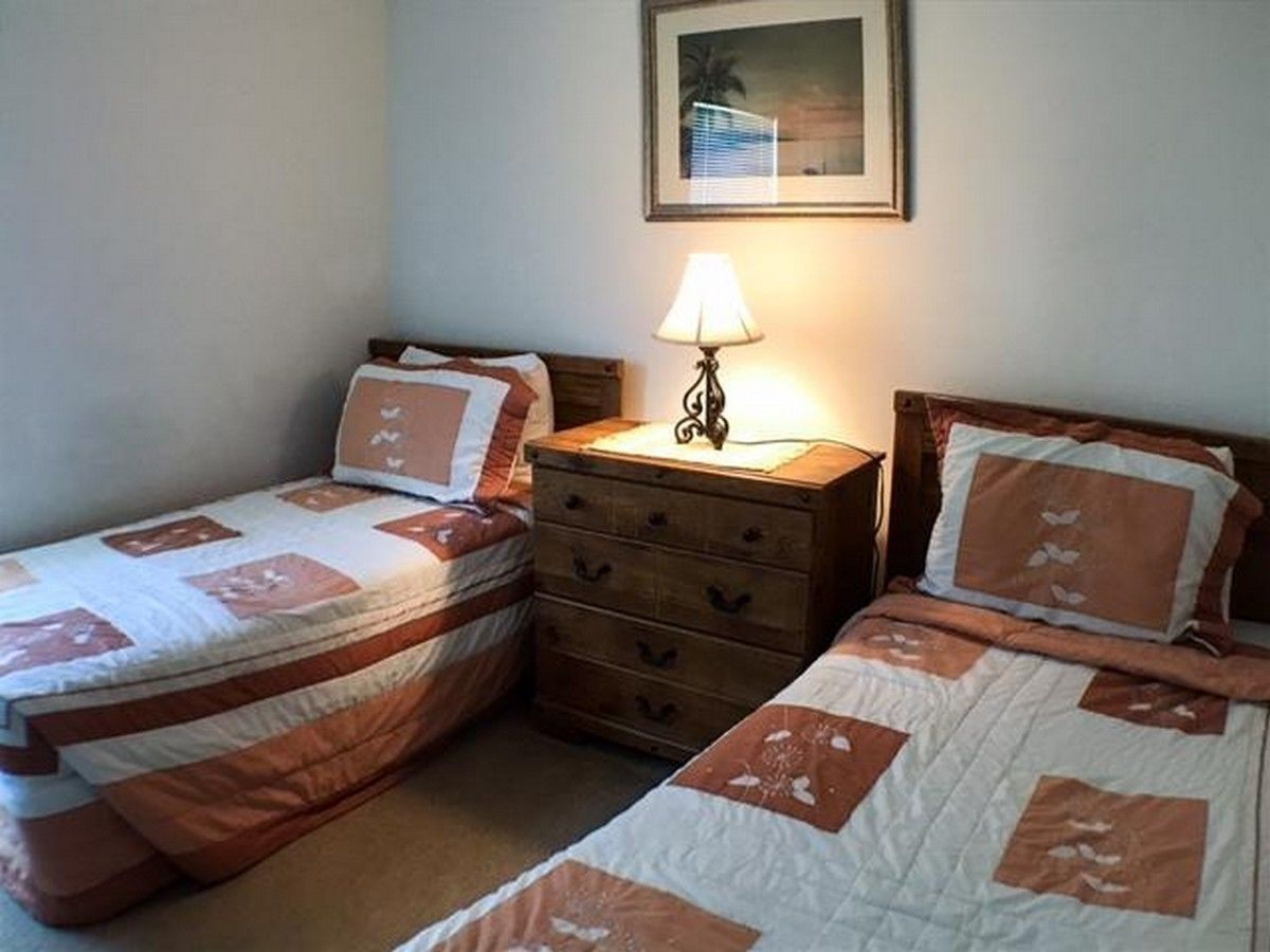 A bedroom with two single beds, a wooden dresser, and a nightstand with a lamp.