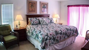 A bedroom with a bed, two nightstands, a chair, and a window with blinds. - Kokomo Golf View Apartment 4 Bedroom (Haines City)