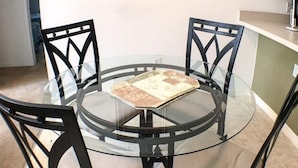 A round glass table with four chairs, a framed picture on the wall, and a kitchen counter in the background. - Kokomo Golf View Apartment 4 Bedroom (Haines City)