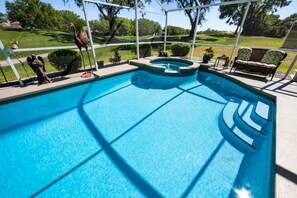 Una piscina con jacuzzi, rodeada por un porche techado con sillas y vistas a un campo de golf.
