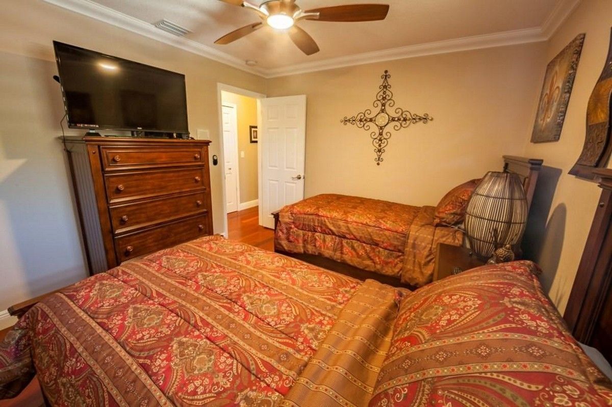 A bedroom with two beds, a dresser, a ceiling fan, a television, and a decorative wall piece.