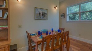 A dining area with a wooden table set for four, surrounded by chairs, with a bookshelf and a painting on the wall. - Camp Palms Indian Pass 2 Bedroom Apartment (Port St. Joe)