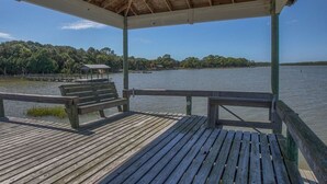 A wooden deck with benches and a covered area overlooking a calm body of water, surrounded by trees. - Camp Palms Indian Pass 2 Bedroom Apartment (Port St. Joe)