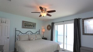 A bedroom with a bed, a ceiling fan, a window with curtains, a door, and a wall clock.
