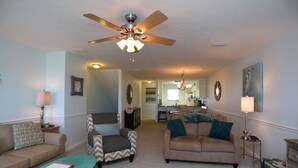 A living room with a ceiling fan, two sofas, a coffee table, and a kitchen in the background.